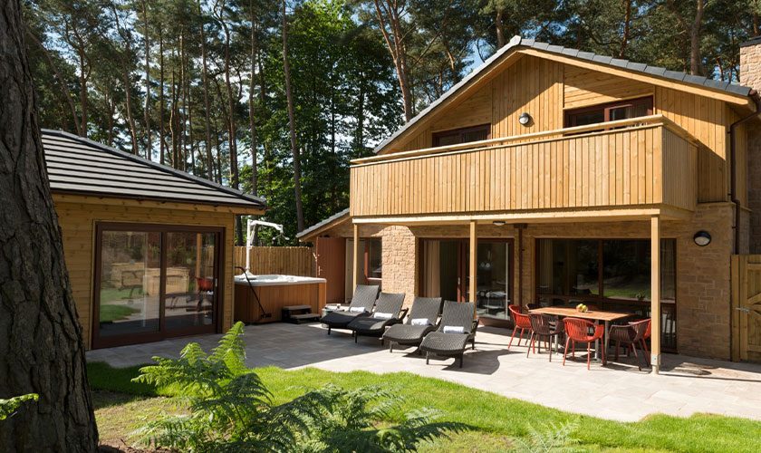 The exterior of an adapted lodge showing sun loungers and a hot tub with hoist.