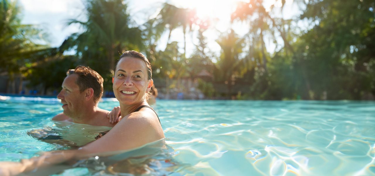 A couple smiling in a pool in the sunshine