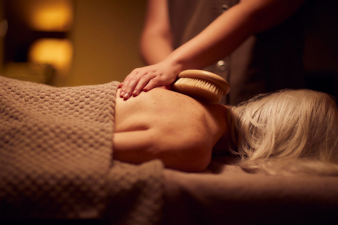 Spa therapist giving a woman a body brush treatment.