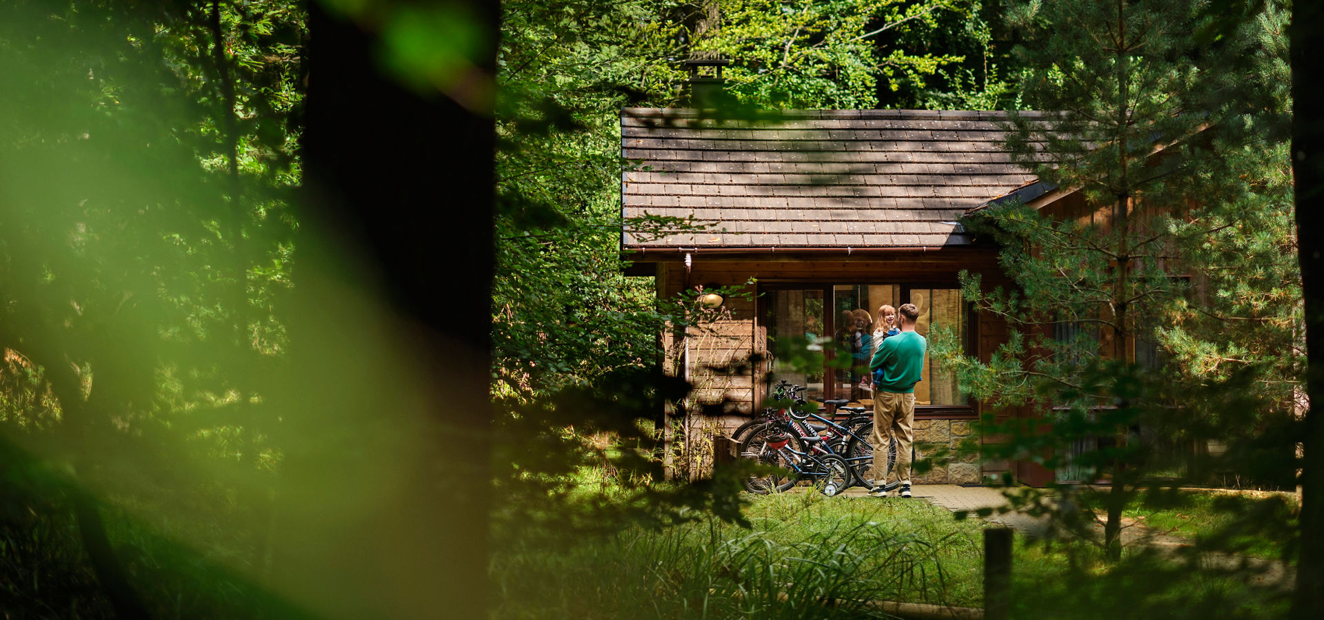 Father and child in the forest, standing outside their lodge.