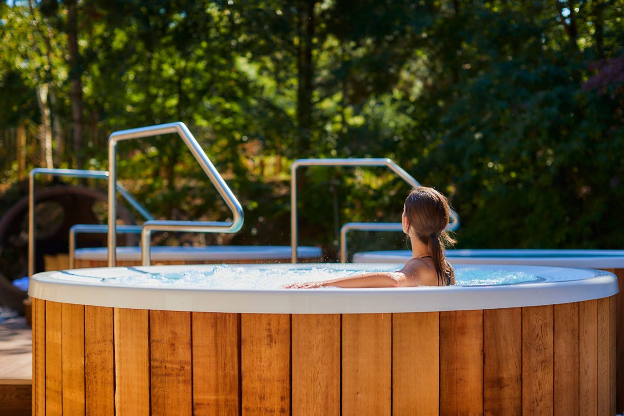 Woman soaking in a bubbling hot tub looking out at the surrounding forest.