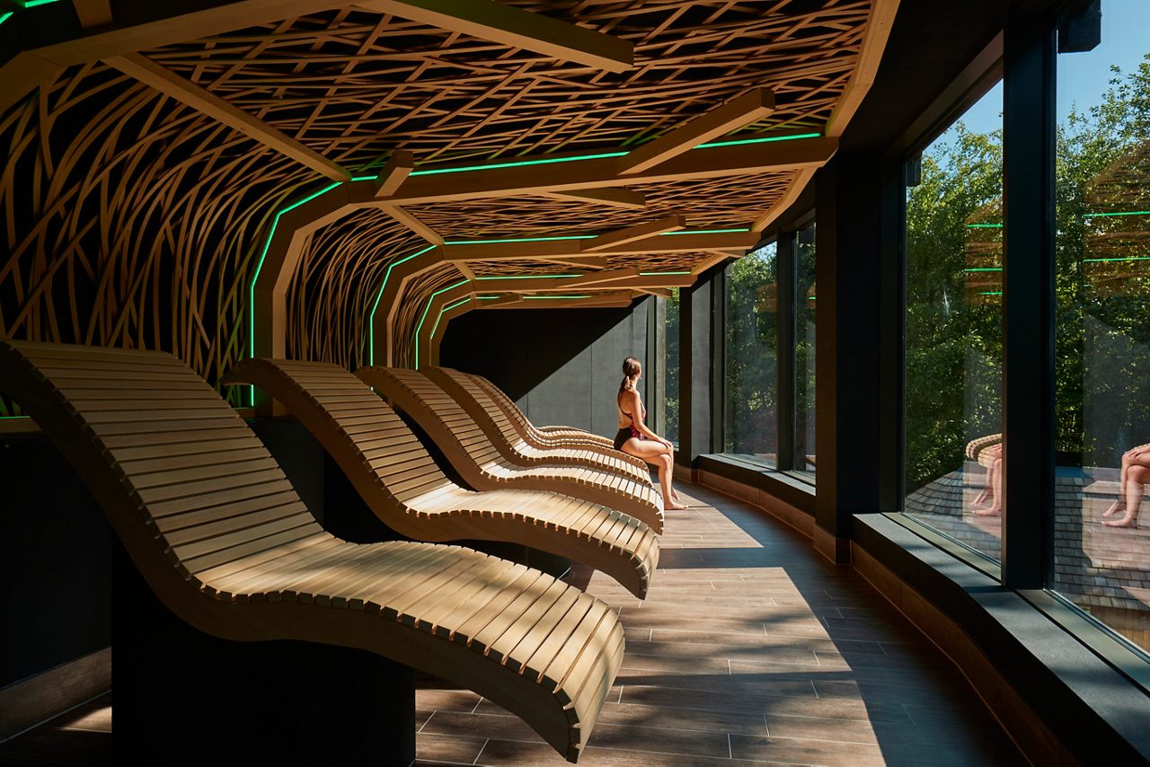 Woman sitting on a contoured wooden seat, looking out at panoramic views of the forest.