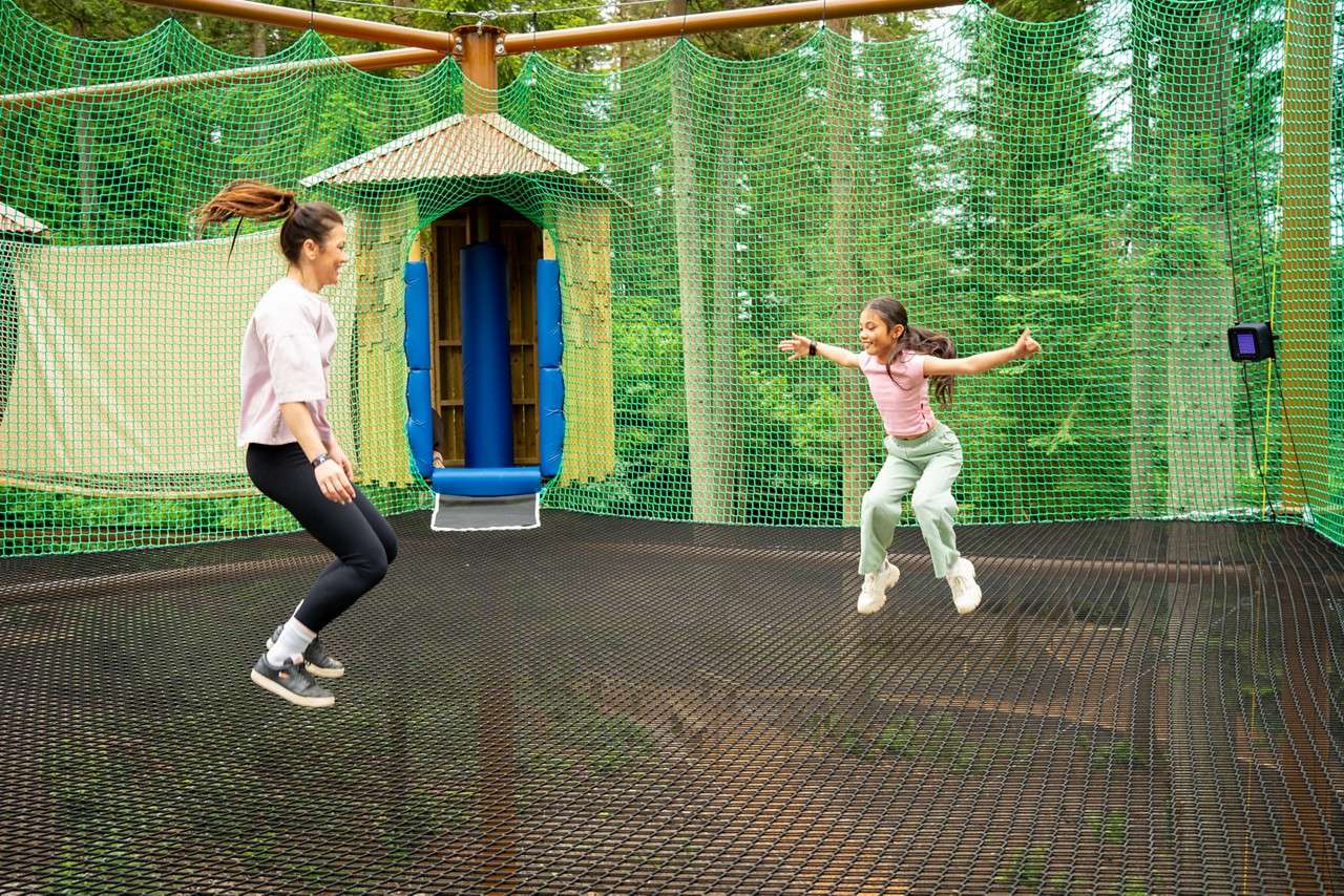 Two teenagers jumping on a suspended net course.