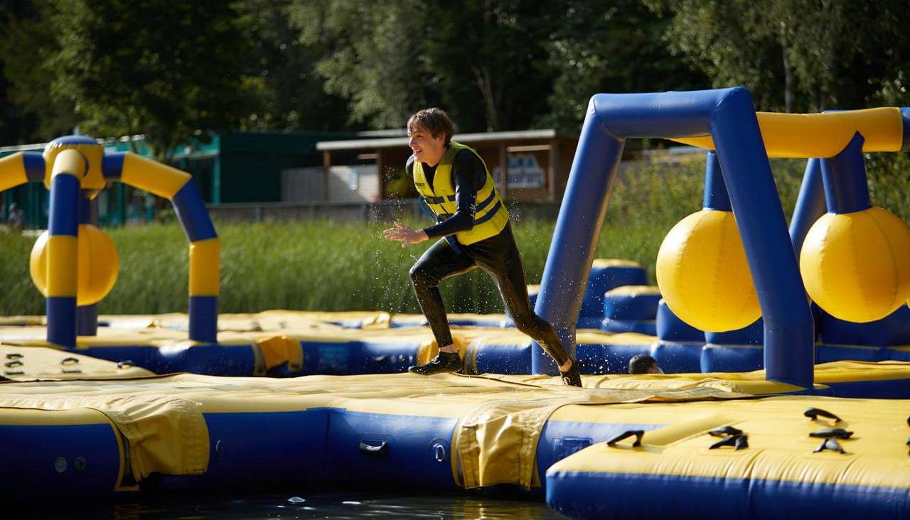 Teenage boy running across an inflatable AquaParc course on the lake.