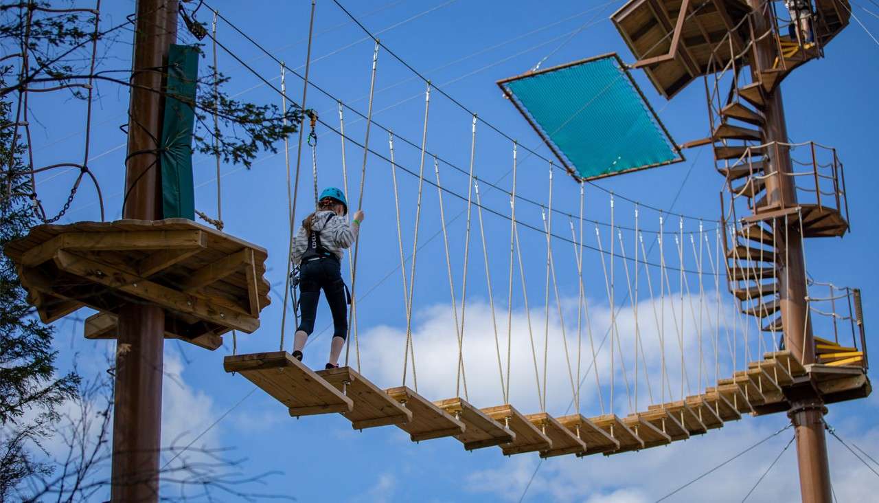 Child climbing a suspended staircase up to a zip line.