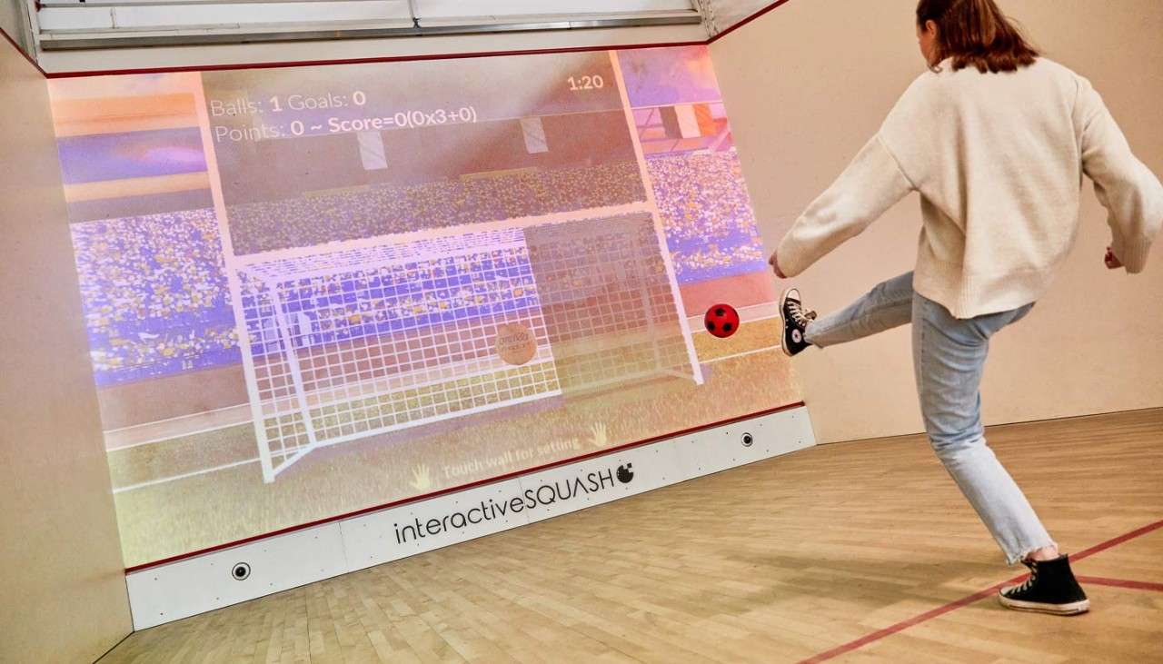 Woman kicking a football at an interactive wall.