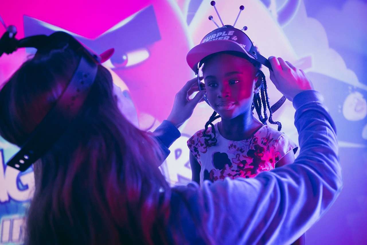 Child wearing a cap and sensor headband is being fitted by an adult, standing before a neon Angry Birds backdrop. Text: “PURPLE POWER 4”.
