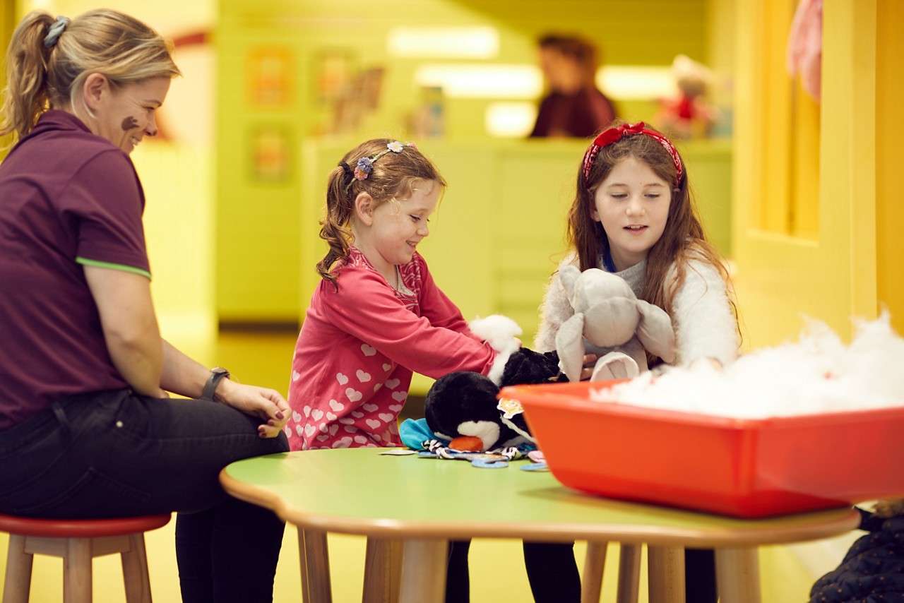 Two young girl making teddy bears with an adult.
