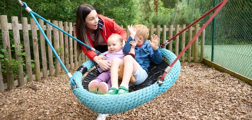 Young boy and a small girl sat in a swing in an outdoor play area.