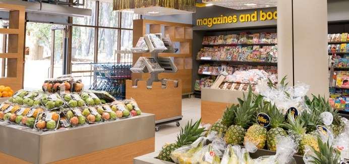 Bagged fruits and pineapples sit on display stands, arranged neatly in a supermarket beside magazine racks. Text: magazines and boo.