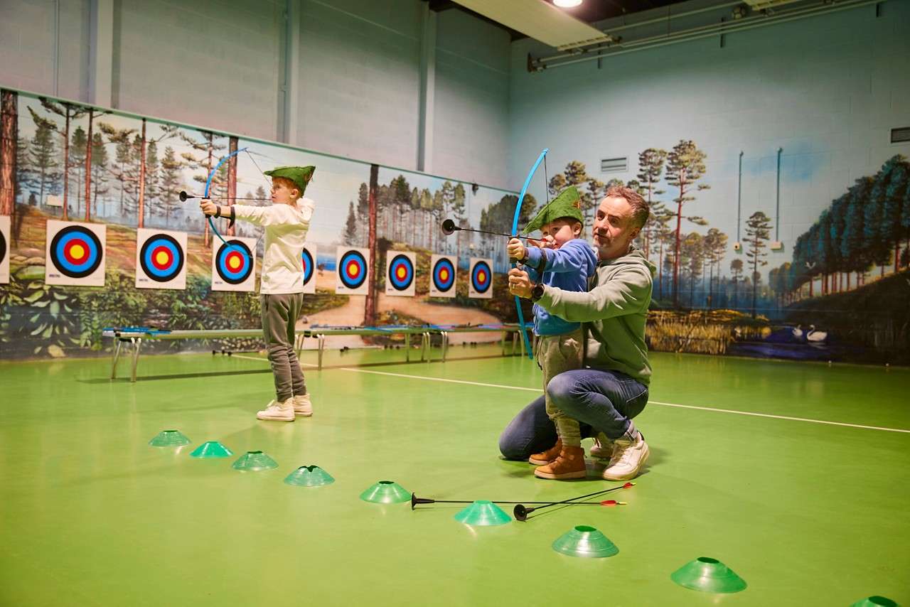 Boy wearing a Robin Hood hat as he aims a bow and arrow at the target.