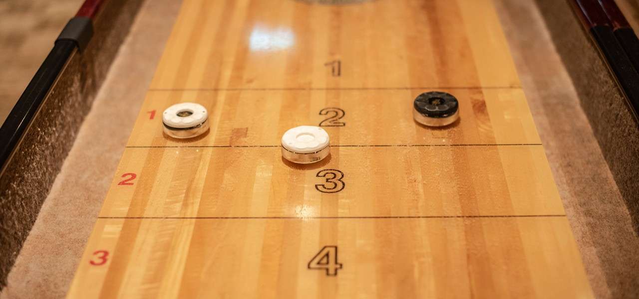 Shuffleboard pucks rest on a varnished board, positioned across scoring lines. Surroundings include felt gutters. Text: centered numbers 1, 2, 3, 4; red left-edge numbers 1, 2, 3.