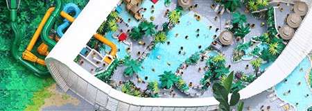 Swimmers wade and play in multiple turquoise pools, surrounded by tropical plants and lounge chairs; a curved white structure and bright water slides frame the bustling indoor waterpark.