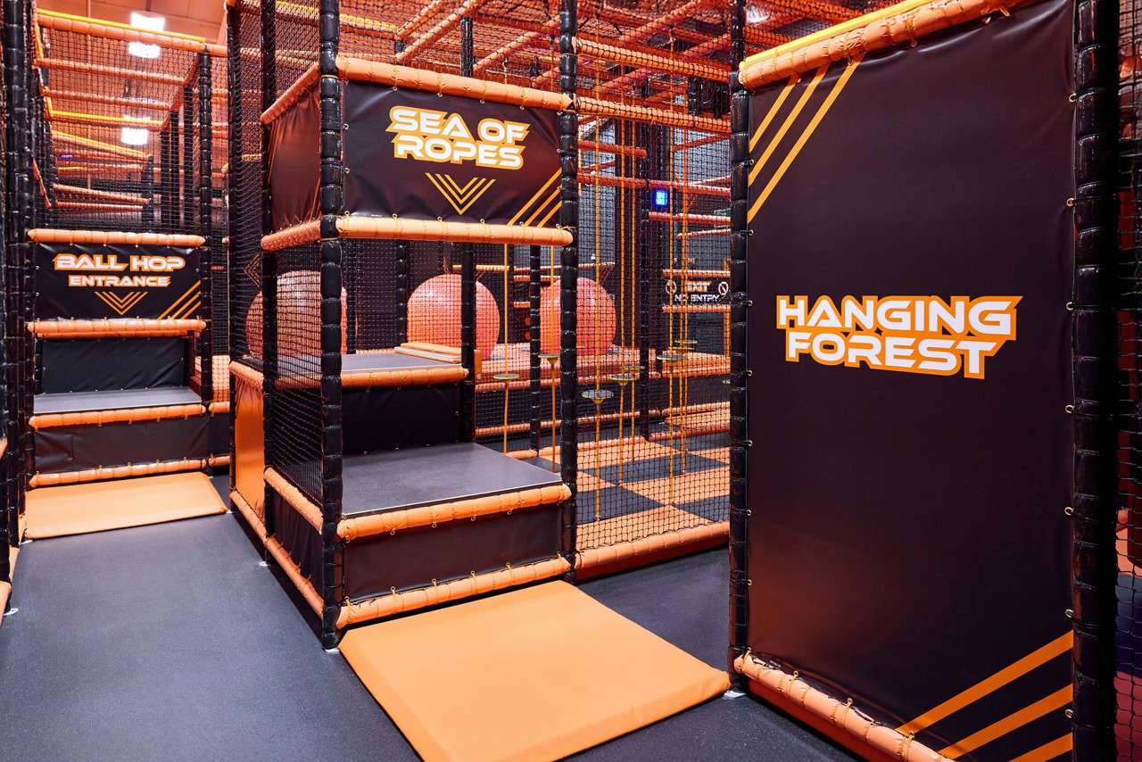 Obstacle-course platforms stand padded and netted; surrounding context is an indoor play area with rope elements and orange fixtures. Text: SEA OF ROPES; BALL HOP ENTRANCE; HANGING FOREST; NO ENTRY.