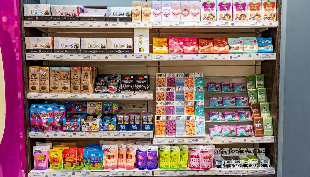 Confectionery shelves display packaged sweets and chocolate bars in a store aisle. Visible text: Creams; Vanilla FUDGE; THE BEST LIQUORICE EVER; PANDA; Choccy Balls; Billie; MOO FREE; HiP Oat Milk Chocolate (Salted Caramel, Cookies No Cream, Salty Pretzel, Orange); BUTTERMILK; JEALOUS SWEETS.