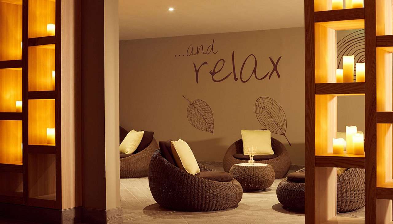 Round wicker lounge chairs cradle cushions, arranged around low tables; warm candlelit shelves glow nearby. On the wall, leaf drawings surround the text: ...and relax.