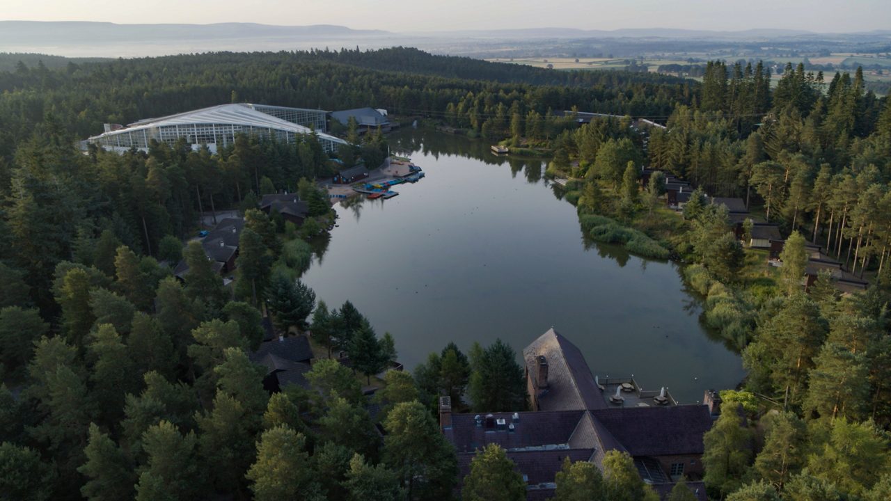 A drone shot showing a lake surrounded by the forest.