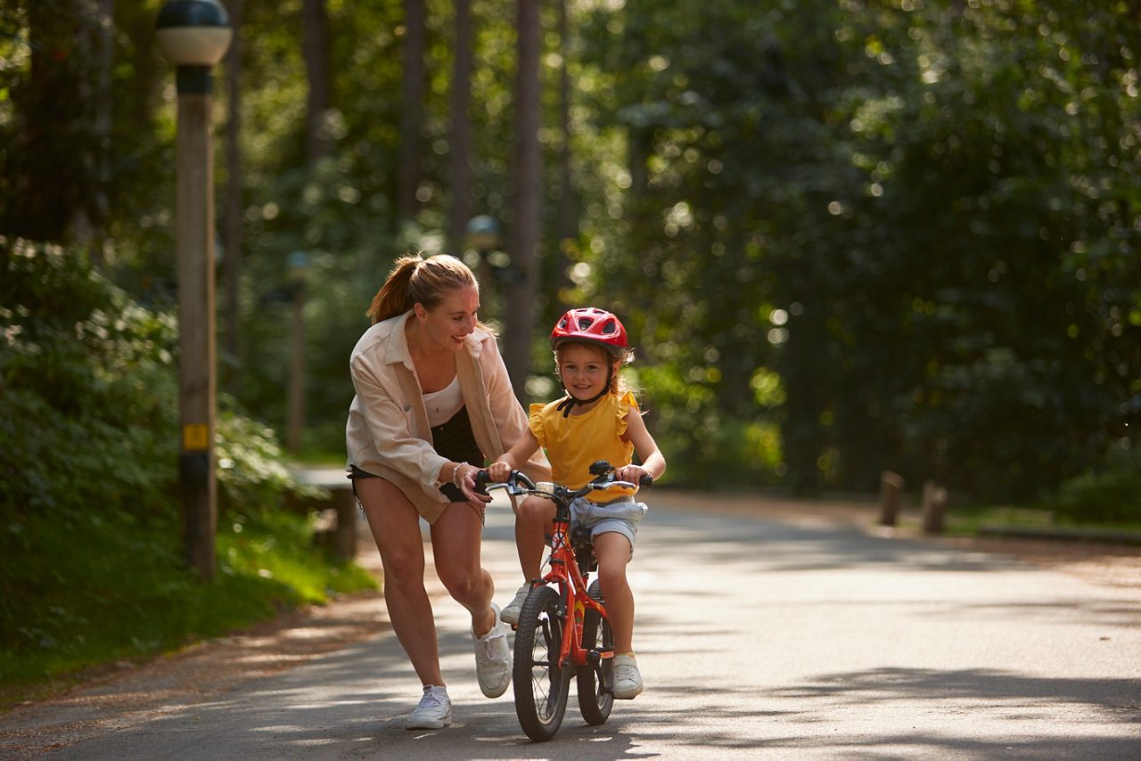 Young girl learning to ride a bike through the forest.