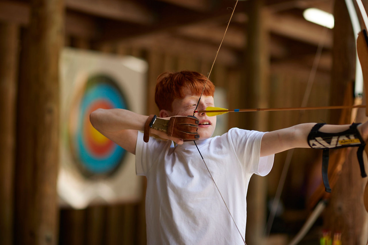 A boy shooting a bow and arrow in the archery activity.