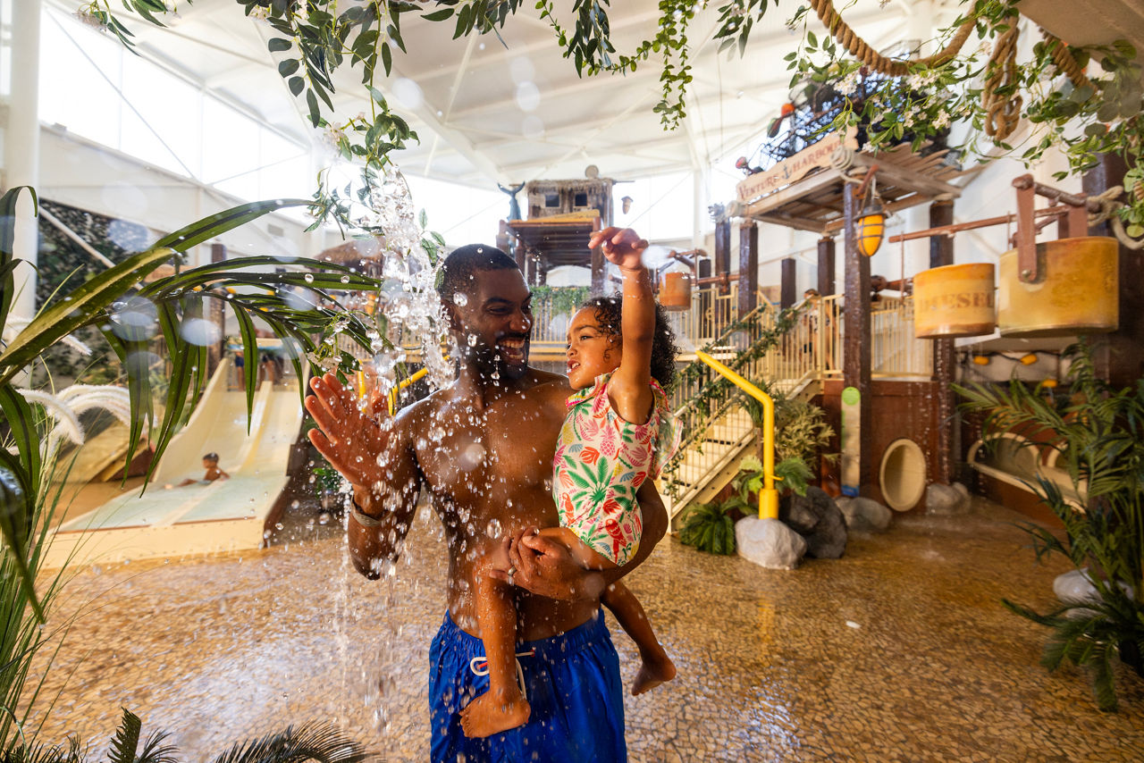Young girl being held by an adult as they splash in the Venture Cove area.